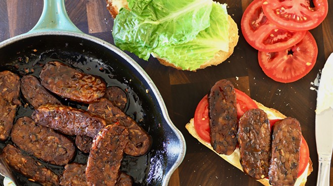 a pan with slices of tempeh next to lettuce and tomatoes
