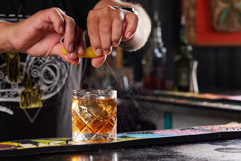 Image: hands squeeze citrus in glass of brown liquid