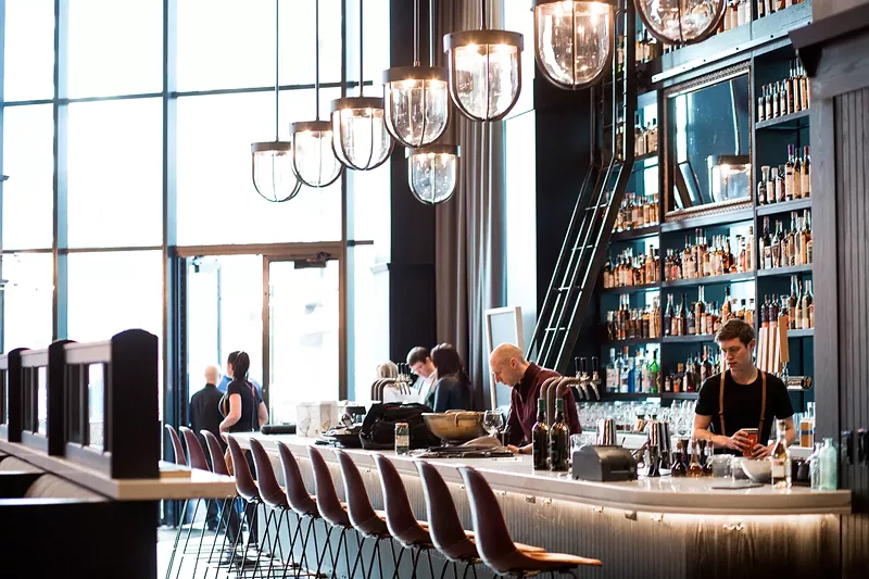 Image: The towering whiskey bar at Hearh & Dram is illuminated by floor-to-ceiling windows at the front of the restaurant.