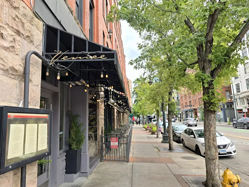 Image: black awning on building next to a sidewalk lined with trees