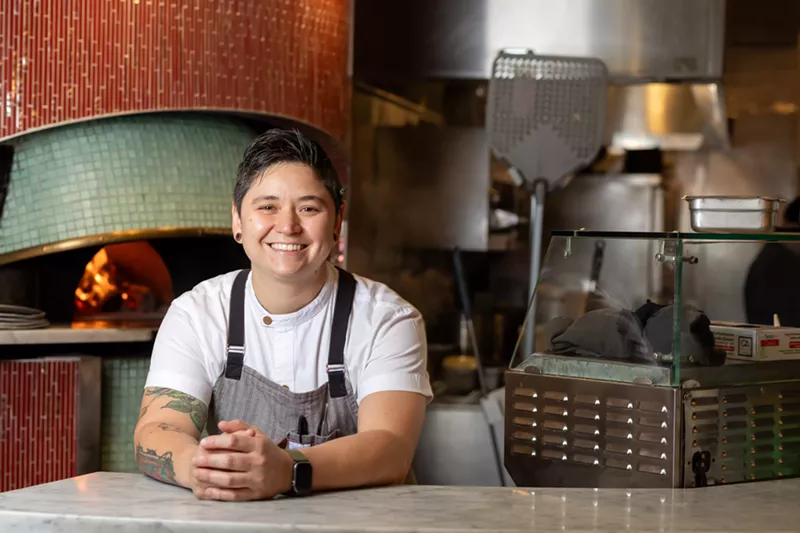Image: person in an apron posing by a good fired oven