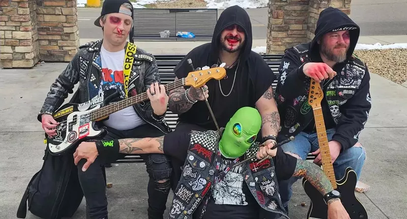 Image: punk bandmates sit on a bench with someone in an alien mask