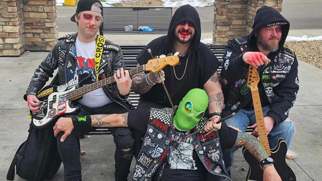 punk bandmates sit on a bench with someone in an alien mask