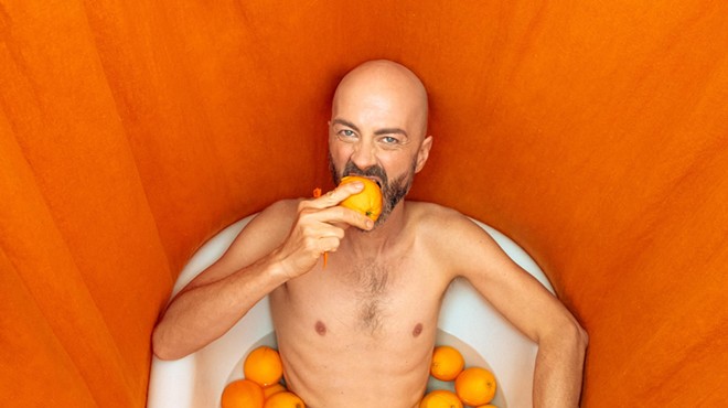man eating an orange in a bathtub filled with oranges