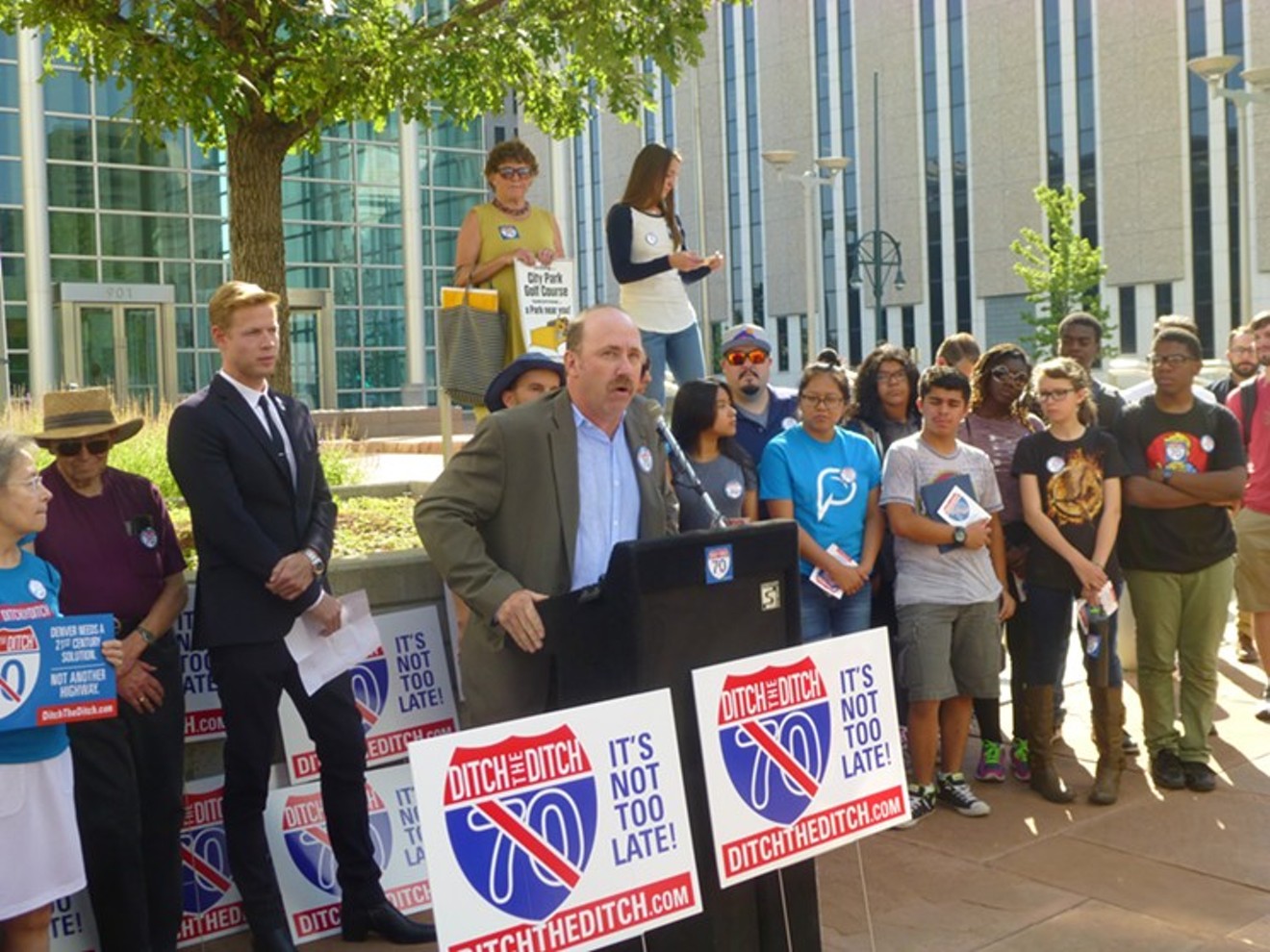 I-70 lawsuit plaintiffs Brad Evans (at podium) and Kyle Zeppelin (in dark suit) rally with supporters at Denver's federal courthouse in July.
