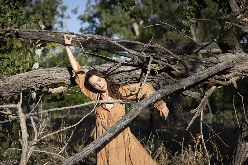 Image: Woman in brown dress standing between branches.