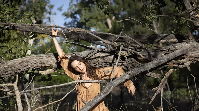 Woman in brown dress standing between branches.