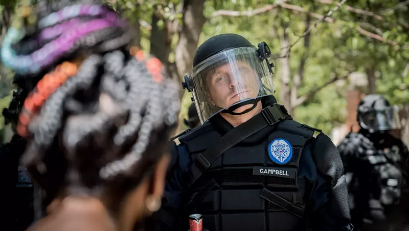 Image: A police officer eyeballing a participant in the June 27 Elijah McClain violin tribute.