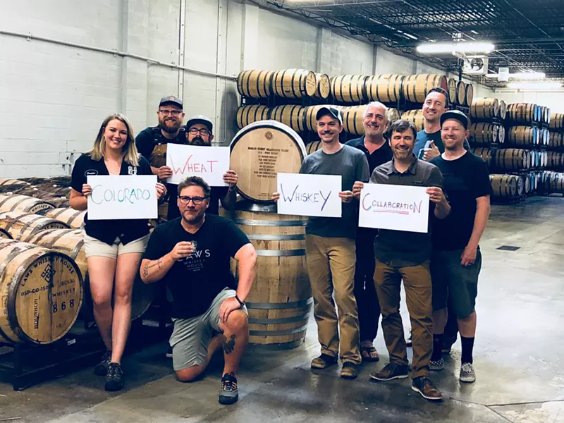 Image: a group of people stand around whiskey barrels holding signs