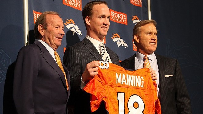 Three men stand in a row, one holding up an orange jersey.