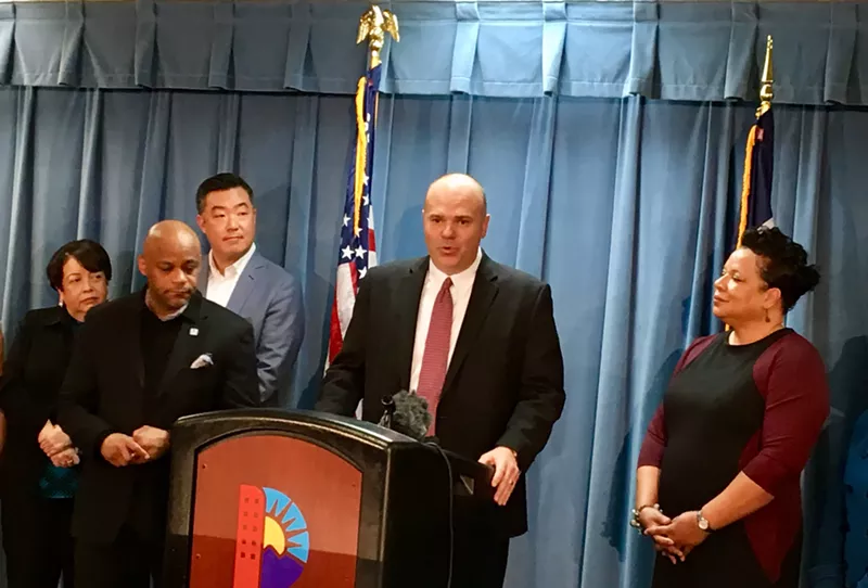 Image: Troy Riggs addresses a crowd of reporters at a press conference.