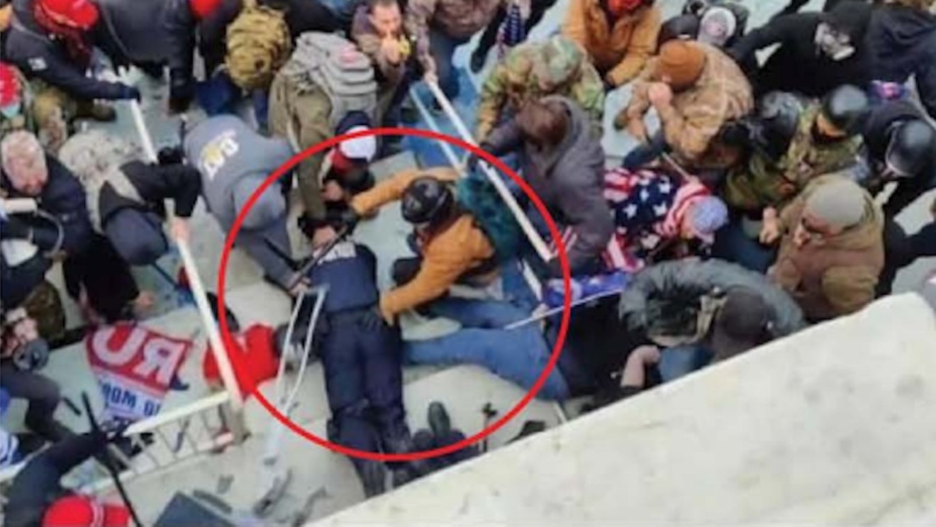 Jeffrey Sabol, in tan jacket and backpack, leans over prone police officer during the January 6 attack on the U.S. Capitol.