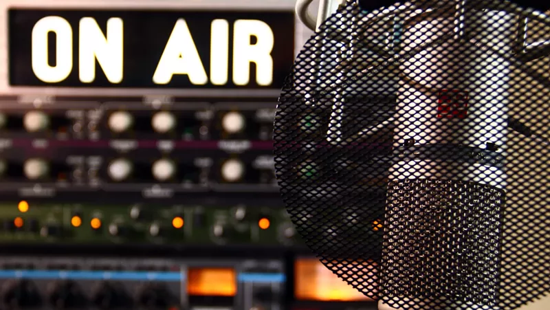 Image: a radio microphone in front of an on air sign