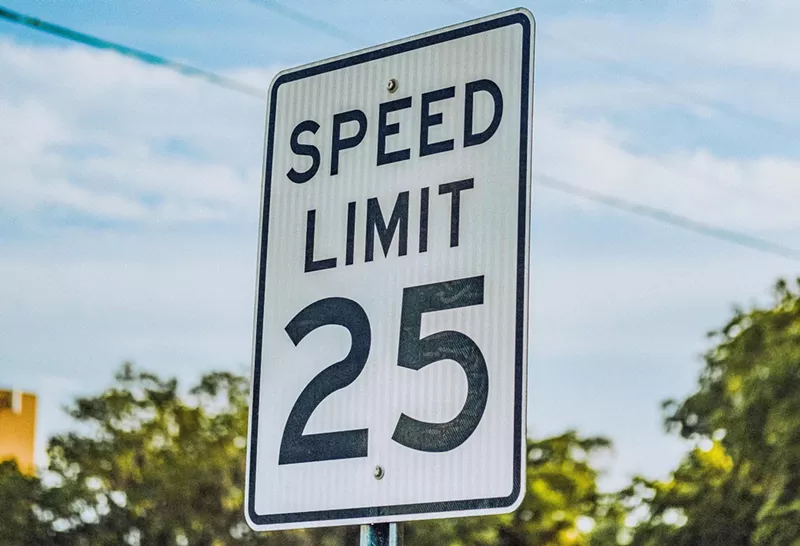 Image: A 25 mph speed limit sign against a blue sky.