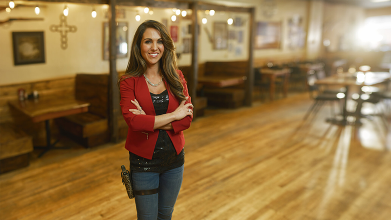 Image: A campaign photo of Lauren Boebert at her Rifle eatery, Shooters Grill, wearing a gun on her hip.