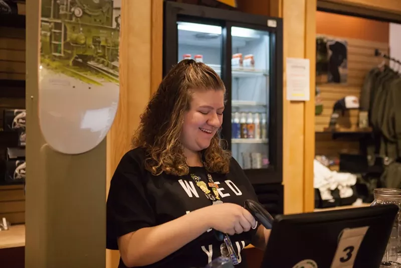 Image: A budtender works the cash register inside an Aurora dispensary.