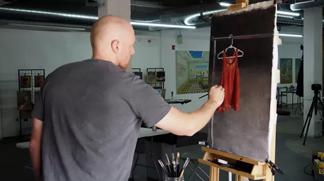 A man works on a painting of an orange dress