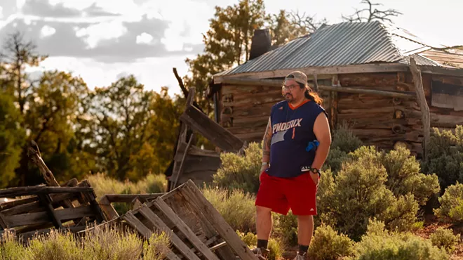 A man dressed in red shorts and a blue shirt stands in a rustic old building.