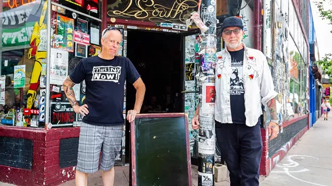 Two men stand in front of store and chalkboard