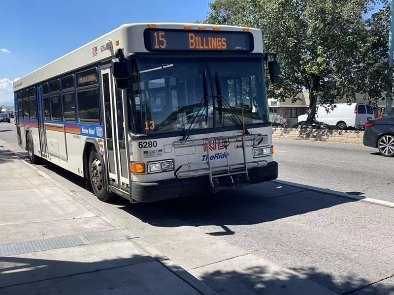 Image: A bus trundles along a day-lit street on Colfax Avenue in Denver.