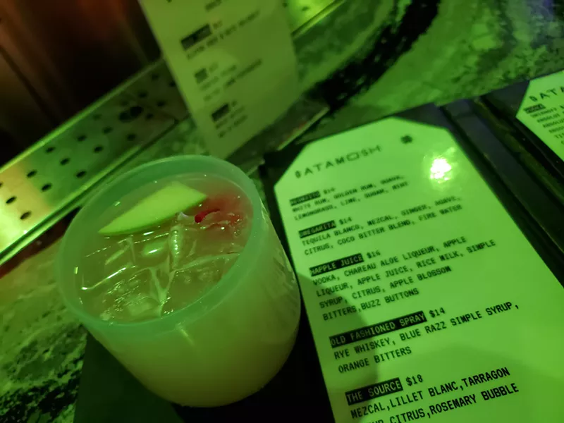 Image: a cocktail next to a menu in green light