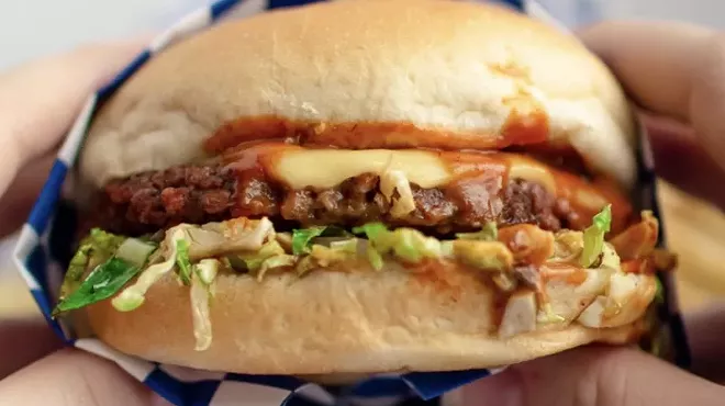 Two hands holding a Meta Burger sandwich featuring a plant-based patty and vegan cheese