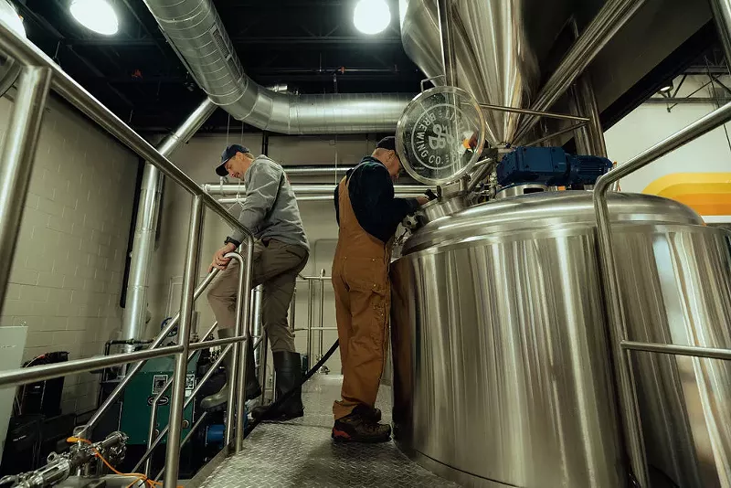 Image: two men near brewing equipment.