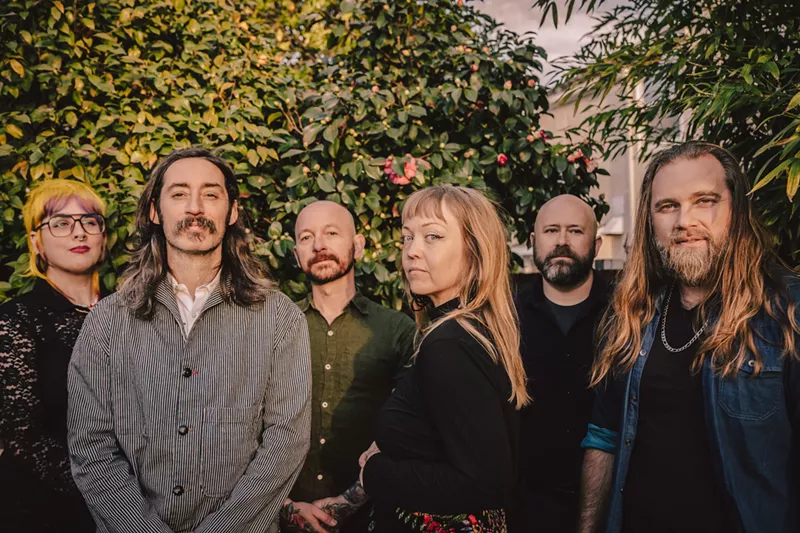 Image: The six current members of indie rock band Murder By Death stand under some greenery.