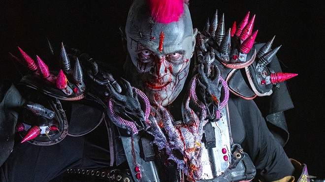 man in zombie facepaint with fake blood has a pink mohawk and is wearing spiky armor