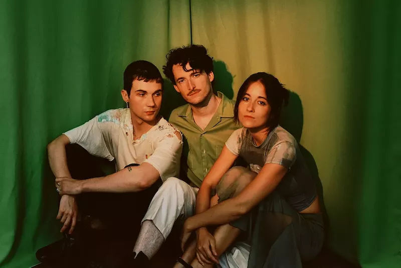 Image: three people sitting on the ground in front of a green curtain