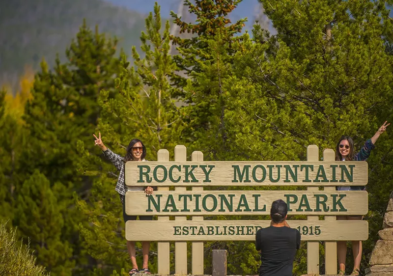 Image: Tourists pose at the west entrance to Rocky Mountain National Park.