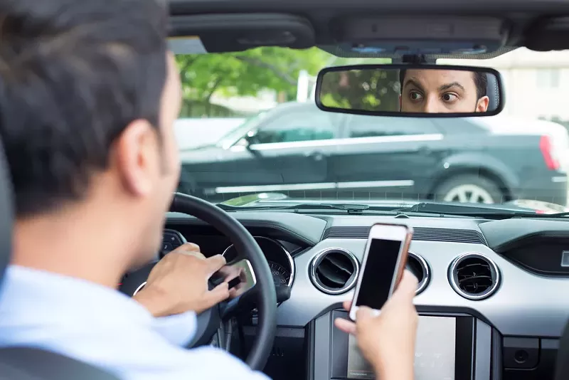 Image: man driving car holding cell phone