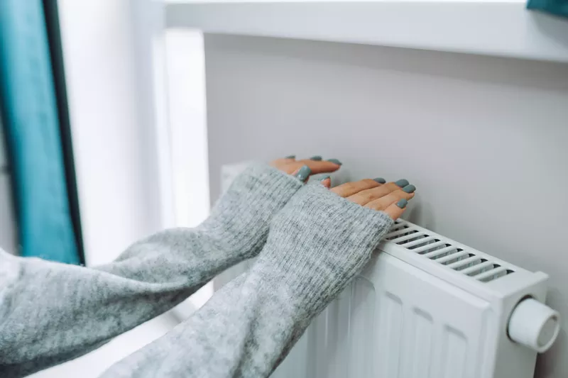 Image: Someone wearing a grey sweater warms their hands on a radiator.