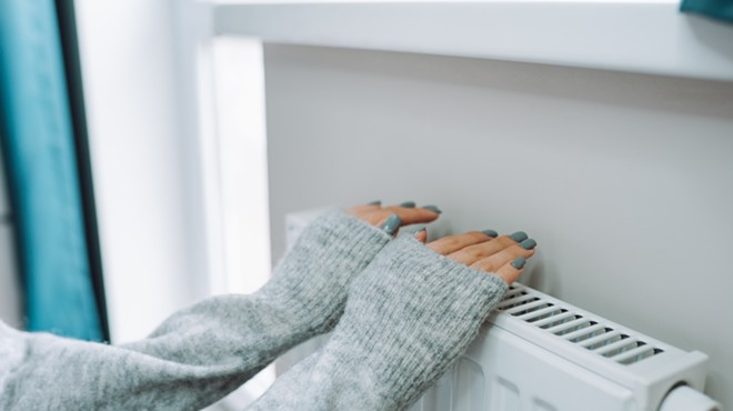 Someone wearing a grey sweater warms their hands on a radiator.