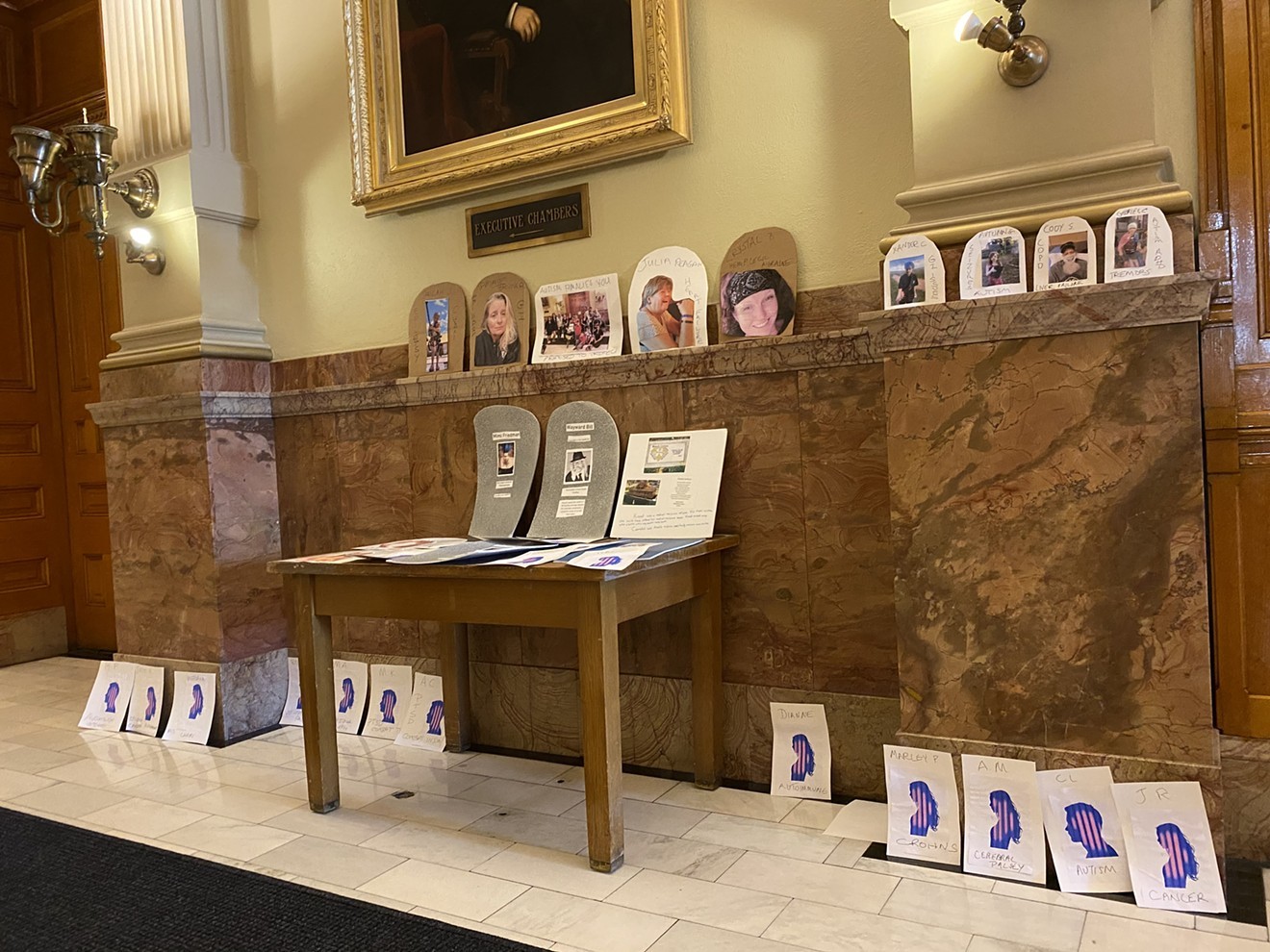 Cards and cardboard gravestones with the faces and names of medical marijuana patients left outside Jared Polis's office.