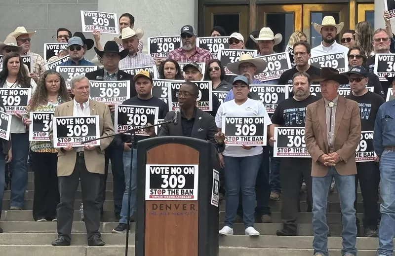 Image: man speaking at podium with crowd behind.