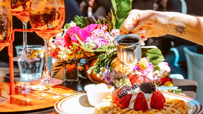 A person drizzling maple syrup on waffles from Steuben's