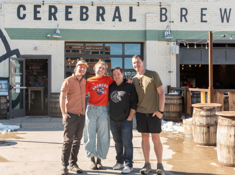 Image: four people posing for a photo in front of a brewery