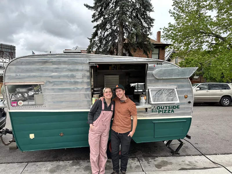 Image: a woman in pink overalls and a man in a brown shirt stand in front of a retro green and white camper