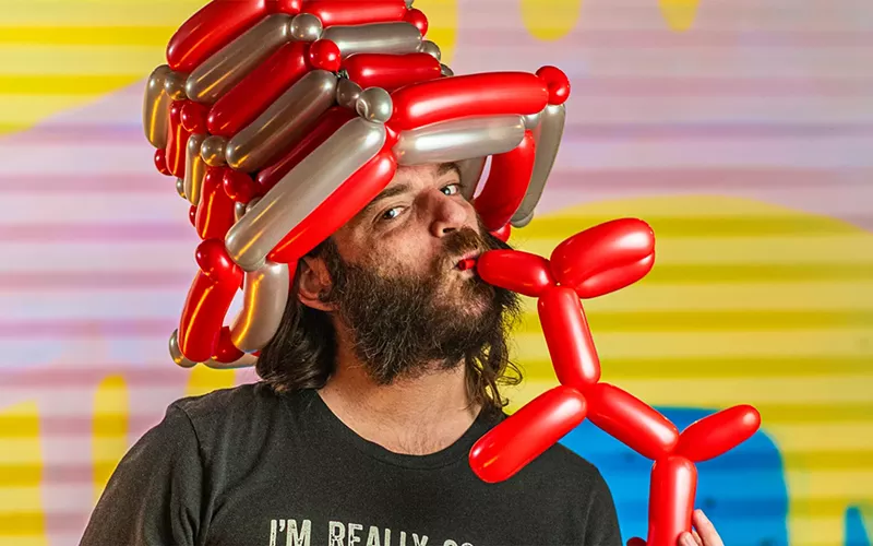 Image: A man kisses a red balloon dog.