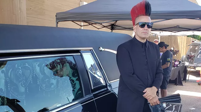 A man with a mohawk stands next to a hearse