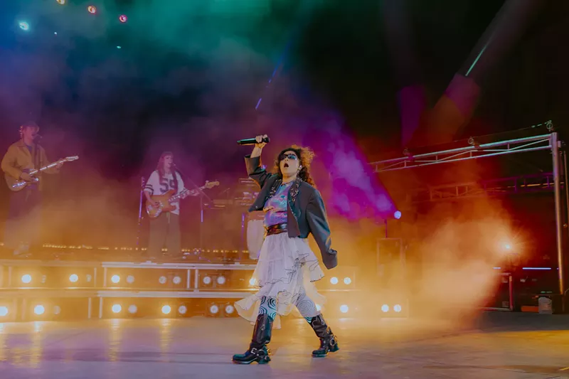 Image: A picture of Remi Wolf performing on stage at Red Rocks with fog and stage lights behind her.