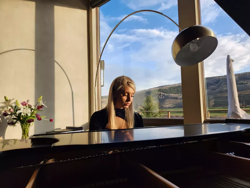 Image: blonde woman playing a baby grand piano.