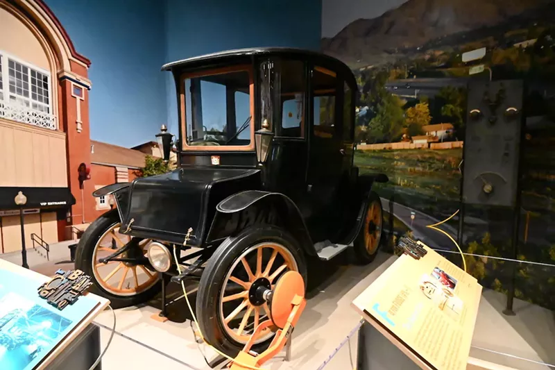 Image: A 1914 Fritchle Electric Colonial Coupe model 283 in History Colorado in front of its charging station with another Denver invention, the boot.