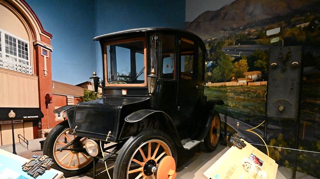 A 1914 Fritchle Electric Colonial Coupe model 283 in History Colorado in front of its charging station with another Denver invention, the boot.