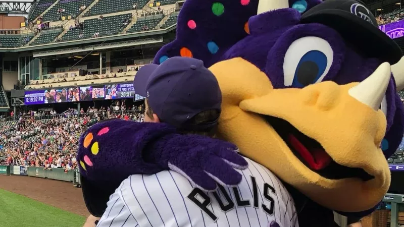 Image: A physical-distancing-free photo of Governor Jared Polis embracing Colorado Rockies mascot Dinger.