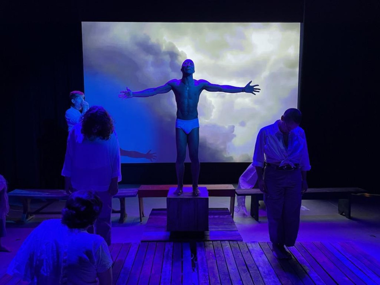 Joshua (Johnathan Underwood) prepares to be crucified while Judas (Emma Maxfield) chokes back tears on stage left, with members of the ensemble between them.