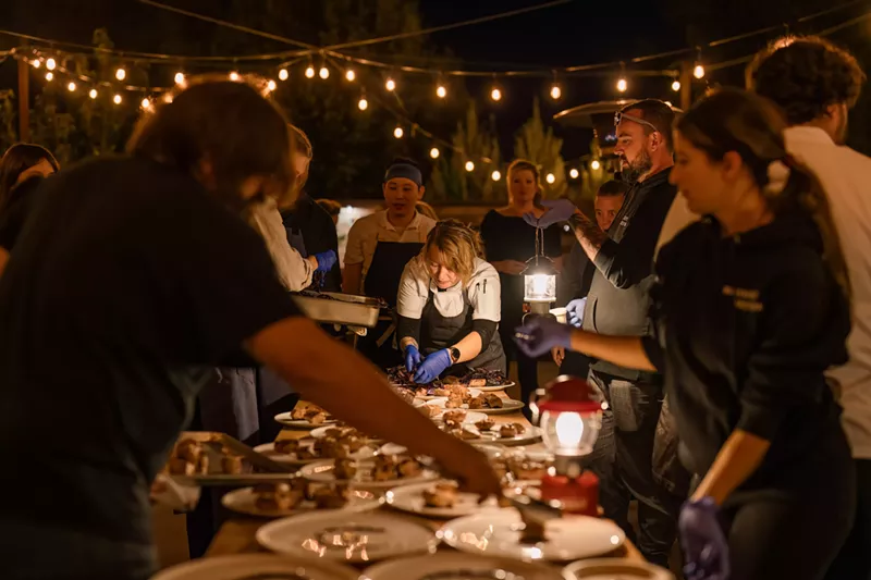 Image: Several chefs around a dimly-lit table, plating a course during Harvest Week