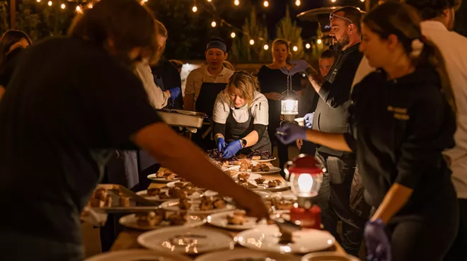 Several chefs around a dimly-lit table, plating a course during Harvest Week