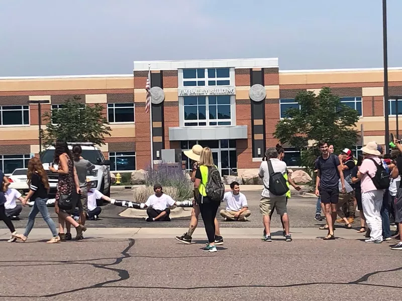 Image: Demonstrators have formed a human chain to block parking lot entrances and exits in front of ICE's Centennial Field Office.